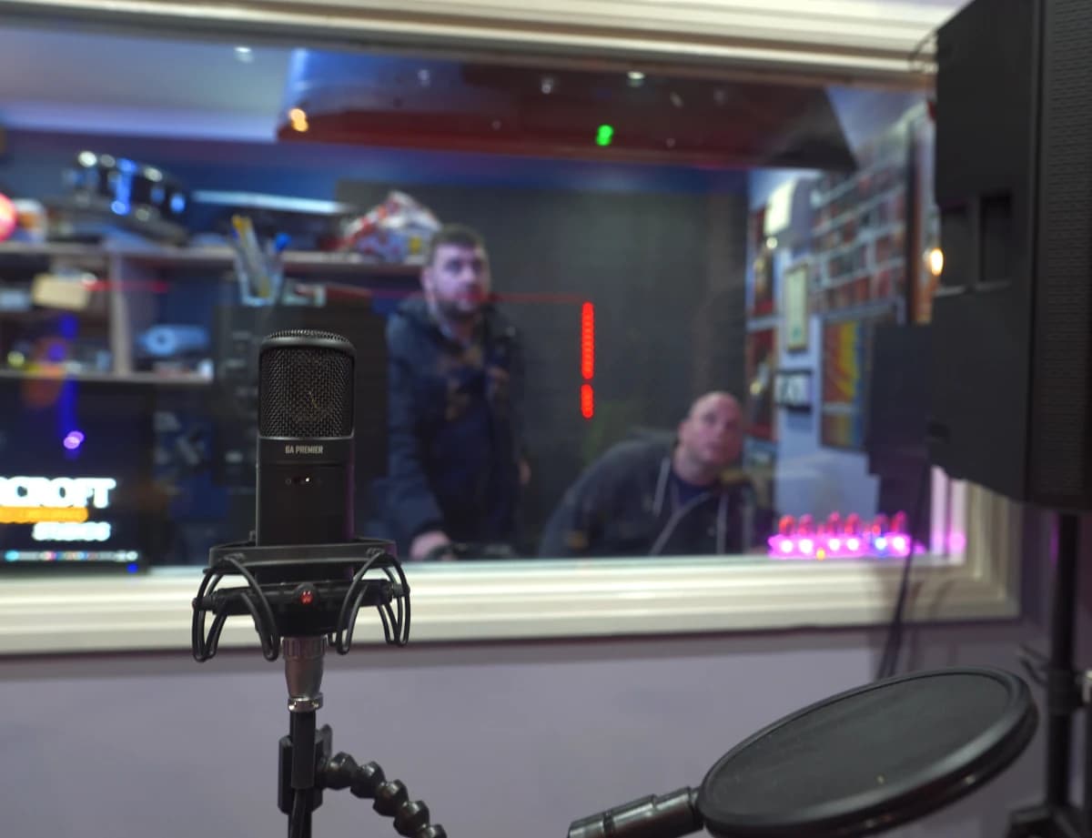 A studio condenser microphone in the control room at Moorcroft Studios, looking through the glass to Tom and an artist in the live room