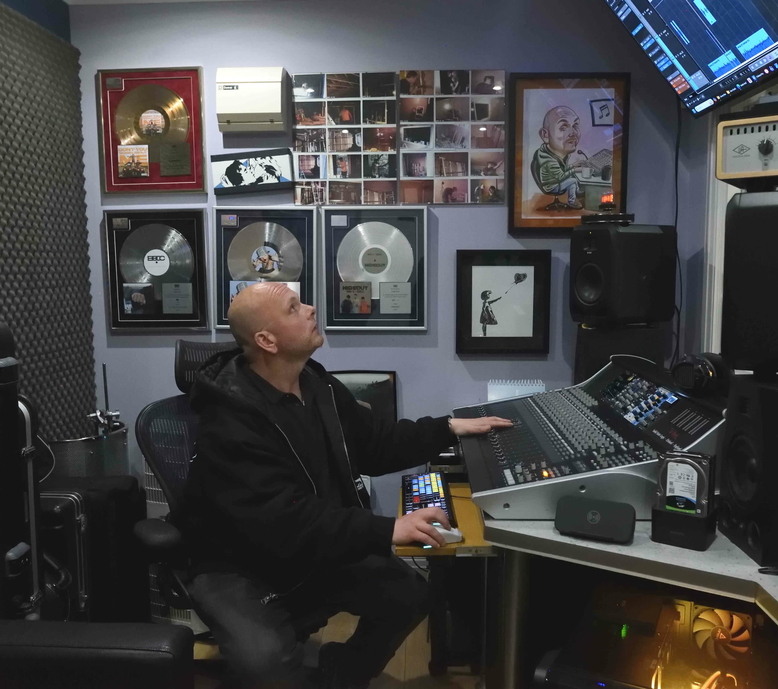 Tom Fox at the SSL mixing console in the Moorcroft Studios control room, looking up at a wall of gold and platinum records